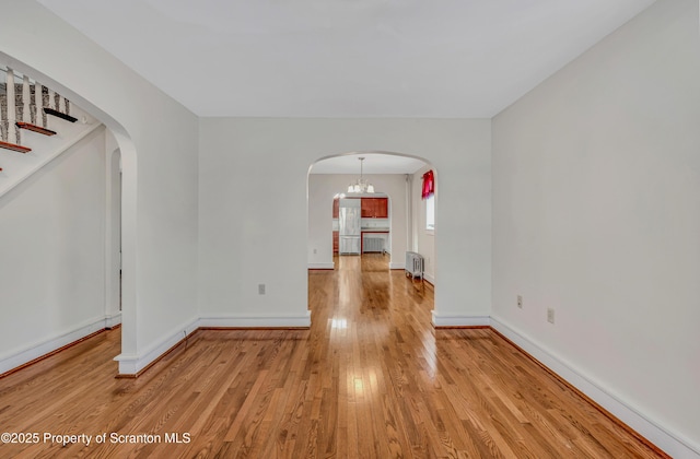 unfurnished room featuring radiator heating unit, a notable chandelier, and light wood-type flooring