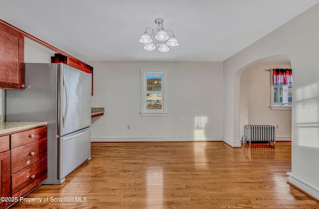 kitchen with a chandelier, radiator heating unit, stainless steel fridge, and light wood-type flooring