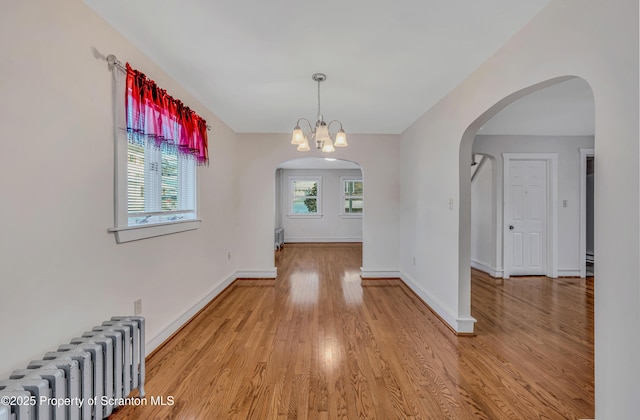 unfurnished dining area featuring a chandelier, radiator, and light hardwood / wood-style floors