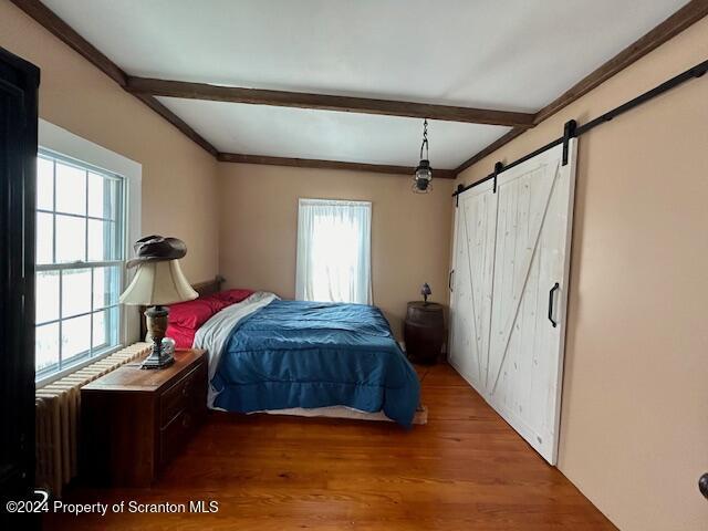 bedroom with beamed ceiling, a barn door, and hardwood / wood-style flooring