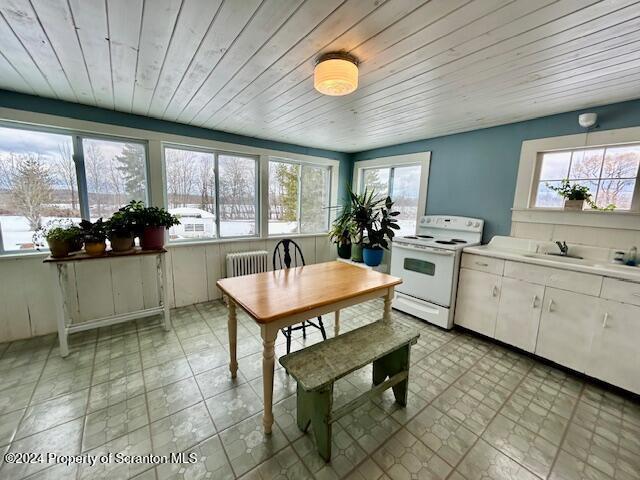 kitchen with radiator heating unit, white cabinetry, white electric stove, and a healthy amount of sunlight