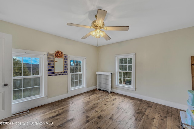 empty room featuring a wealth of natural light, radiator heating unit, and hardwood / wood-style floors