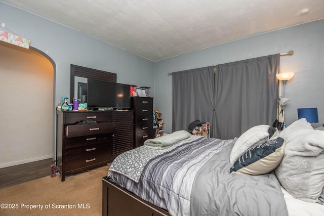 bedroom featuring light colored carpet, arched walkways, and baseboards