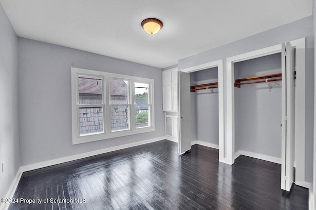 unfurnished bedroom with dark hardwood / wood-style flooring and two closets