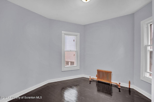 unfurnished room featuring dark hardwood / wood-style floors and radiator heating unit