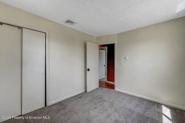unfurnished bedroom featuring carpet floors, a closet, baseboards, visible vents, and a textured ceiling