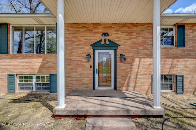 doorway to property featuring covered porch and brick siding