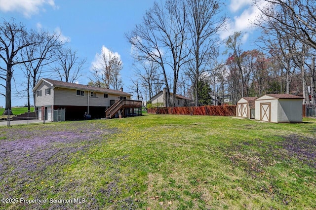 view of yard with a wooden deck, an outdoor structure, a fenced backyard, a shed, and stairs