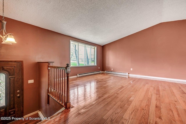 interior space with baseboard heating, light wood-style flooring, a textured ceiling, and lofted ceiling