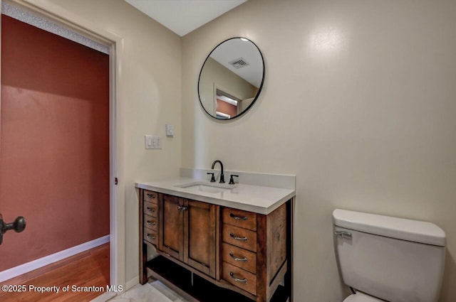 bathroom with wood finished floors, toilet, vanity, baseboards, and visible vents