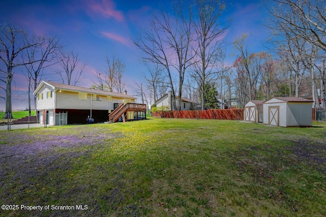 yard at dusk featuring stairs, a shed, a wooden deck, and a fenced backyard