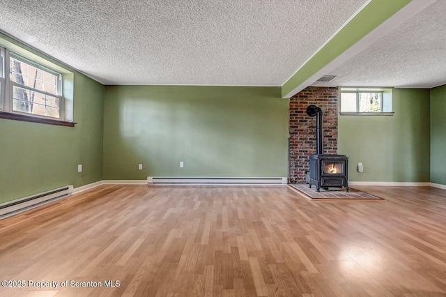 unfurnished living room featuring a baseboard heating unit, a wood stove, a textured ceiling, and wood finished floors