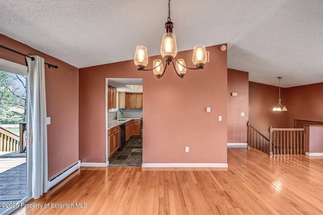 unfurnished dining area featuring a textured ceiling, light wood-style flooring, a sink, a baseboard radiator, and vaulted ceiling