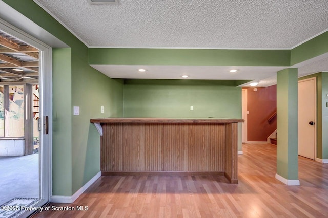 bar with a textured ceiling, a bar, wood finished floors, and baseboards