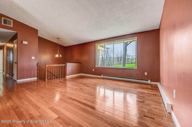unfurnished room featuring a textured ceiling, visible vents, light wood finished floors, and a baseboard heating unit