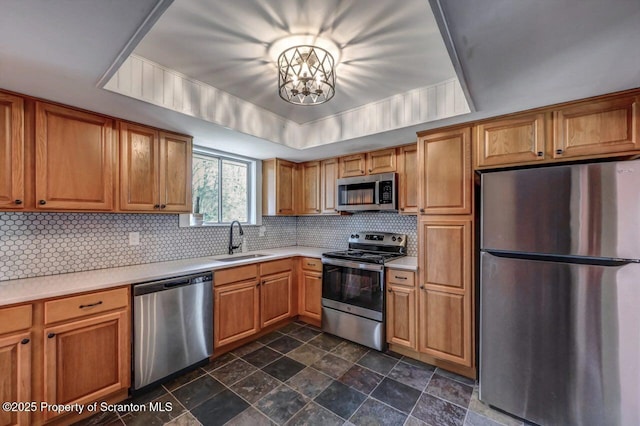 kitchen with decorative backsplash, stainless steel appliances, stone finish floor, light countertops, and a sink