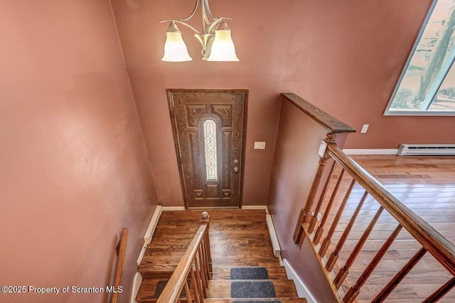 entrance foyer with wood finished floors, a notable chandelier, a baseboard heating unit, and baseboards