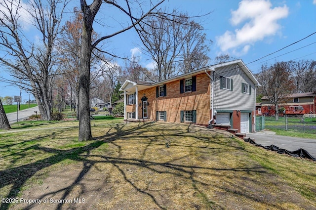 raised ranch featuring a front lawn, a garage, driveway, brick siding, and fence