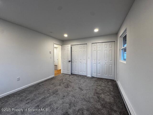 unfurnished bedroom featuring dark colored carpet and multiple closets