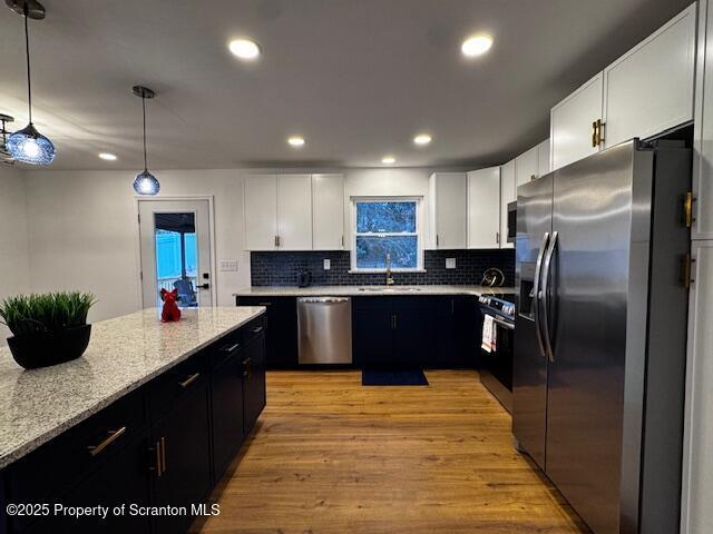 kitchen with backsplash, white cabinets, sink, hanging light fixtures, and appliances with stainless steel finishes