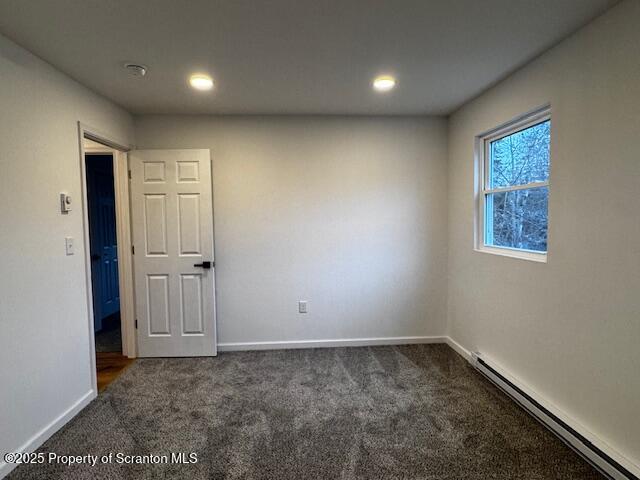 carpeted spare room featuring a baseboard heating unit