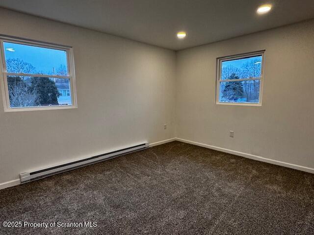 unfurnished room featuring dark carpet and a baseboard heating unit