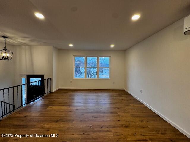 unfurnished living room featuring dark hardwood / wood-style flooring, an AC wall unit, and an inviting chandelier