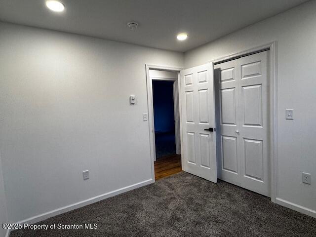 unfurnished bedroom featuring dark colored carpet and a closet