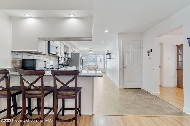 kitchen with light hardwood / wood-style floors, kitchen peninsula, a breakfast bar area, stainless steel appliances, and white cabinets