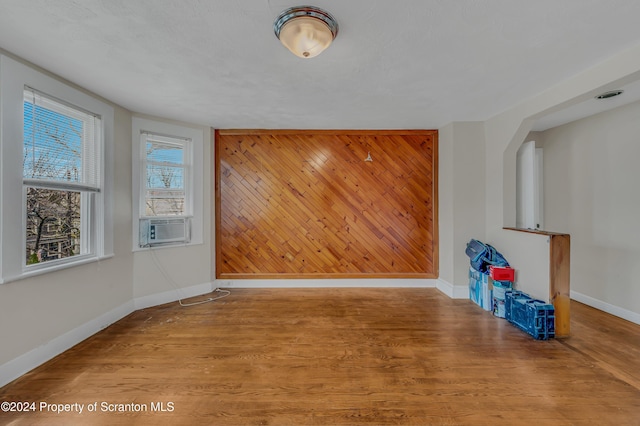 empty room featuring wood walls, cooling unit, and light wood-type flooring