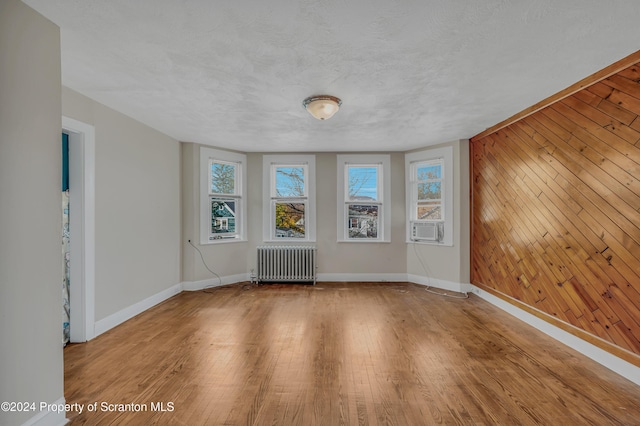 spare room featuring hardwood / wood-style floors, cooling unit, wooden walls, a textured ceiling, and radiator heating unit