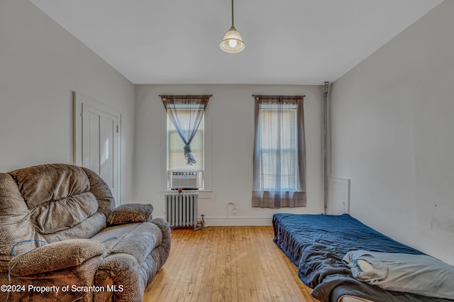 bedroom with radiator heating unit, cooling unit, and wood-type flooring