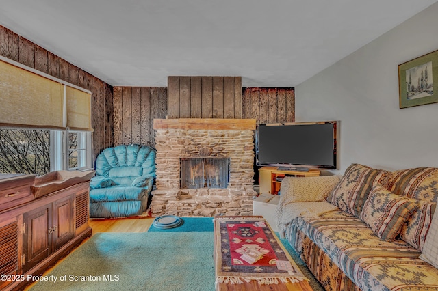 living room featuring a stone fireplace, wood walls, and wood finished floors