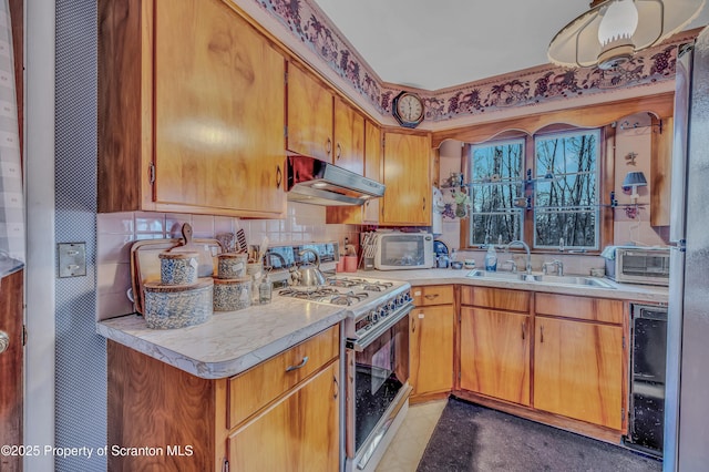 kitchen featuring light countertops, gas range oven, a sink, and under cabinet range hood