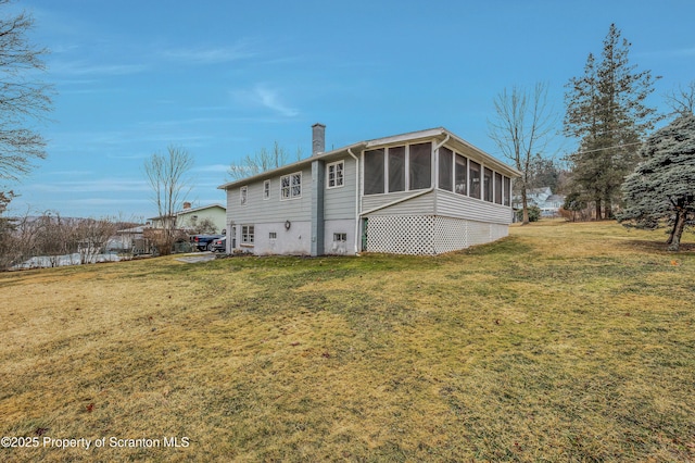 rear view of property featuring a yard, a chimney, and a sunroom