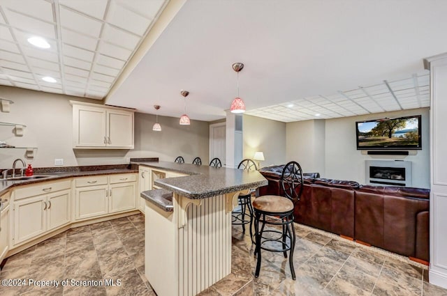 kitchen with a paneled ceiling, a breakfast bar, sink, pendant lighting, and cream cabinetry