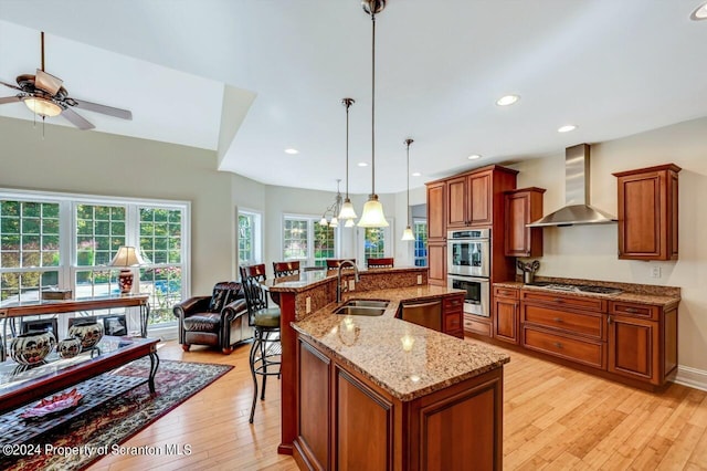 kitchen with stainless steel appliances, sink, wall chimney range hood, pendant lighting, and a large island with sink