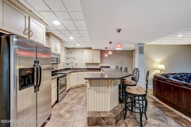 kitchen with a kitchen breakfast bar, sink, appliances with stainless steel finishes, cream cabinetry, and decorative light fixtures