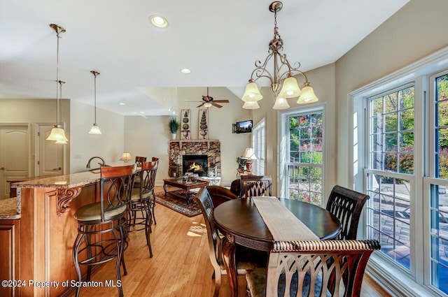 dining space featuring a fireplace, ceiling fan with notable chandelier, and light hardwood / wood-style flooring