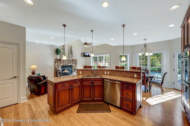 kitchen featuring sink, stainless steel dishwasher, an island with sink, decorative light fixtures, and light wood-type flooring