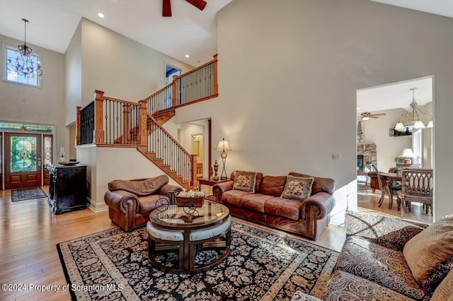 living room featuring ceiling fan with notable chandelier, light wood-type flooring, and a towering ceiling