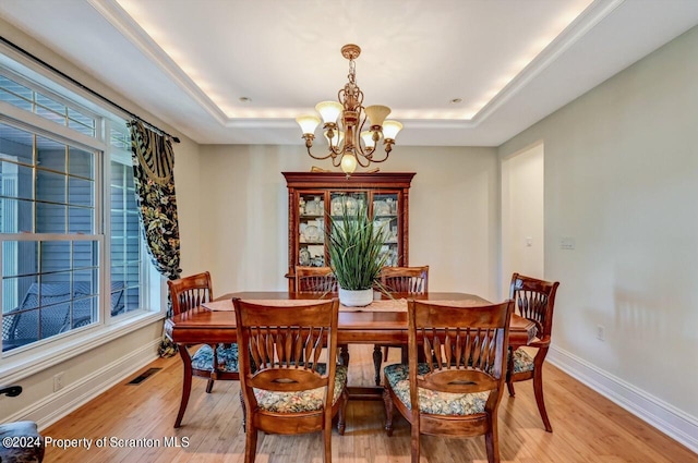 dining area featuring light hardwood / wood-style floors, a raised ceiling, and a chandelier