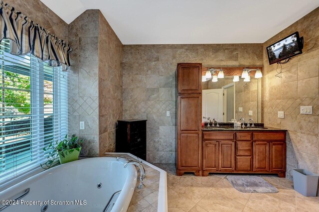 bathroom with tiled tub, tile patterned flooring, vanity, and tile walls