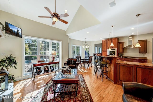 living room featuring ceiling fan with notable chandelier, light wood-type flooring, a wealth of natural light, and vaulted ceiling