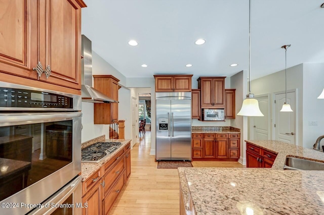 kitchen with light stone countertops, sink, stainless steel appliances, wall chimney range hood, and decorative light fixtures