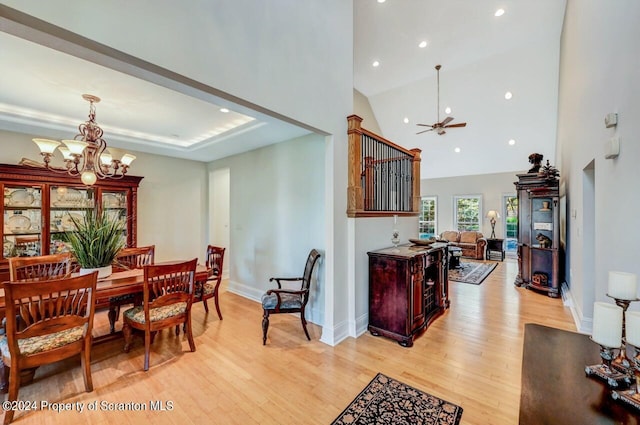 dining area with ceiling fan with notable chandelier, light wood-type flooring, and high vaulted ceiling