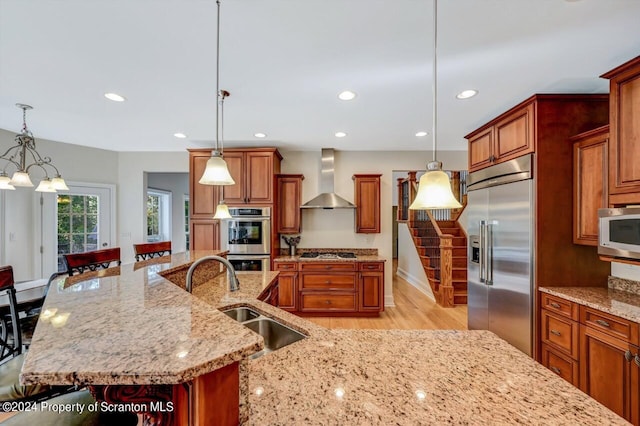 kitchen featuring pendant lighting, a large island with sink, sink, wall chimney exhaust hood, and appliances with stainless steel finishes