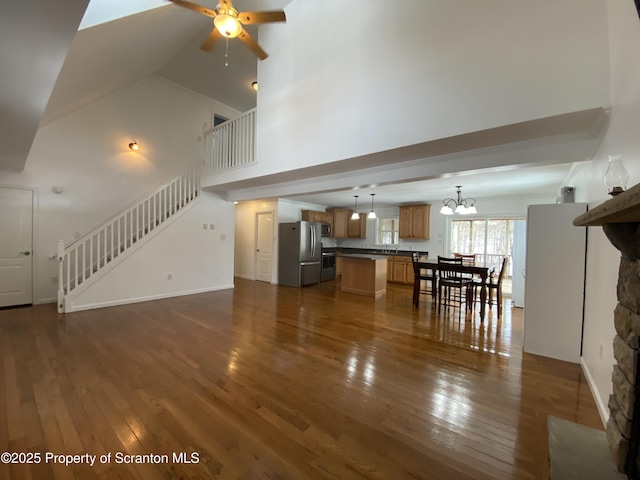 unfurnished living room with dark wood-type flooring, a stone fireplace, and ceiling fan with notable chandelier