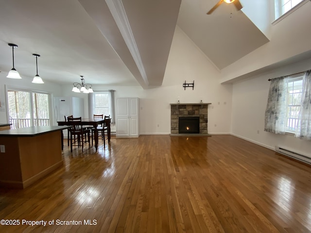 living room with vaulted ceiling, a stone fireplace, dark hardwood / wood-style floors, a baseboard radiator, and ceiling fan