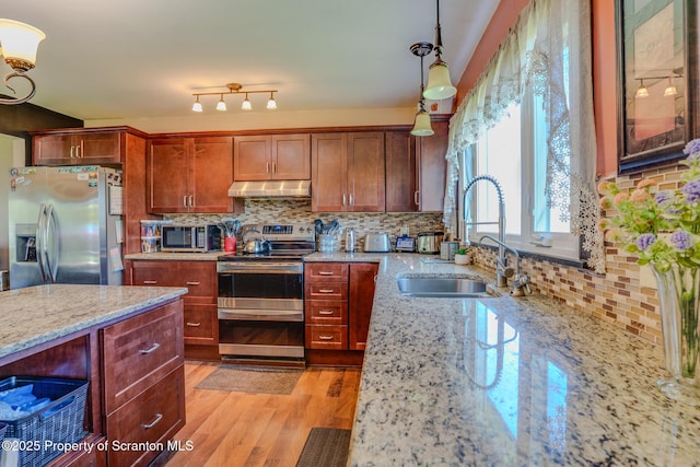 kitchen featuring decorative backsplash, a sink, light stone counters, under cabinet range hood, and stainless steel appliances